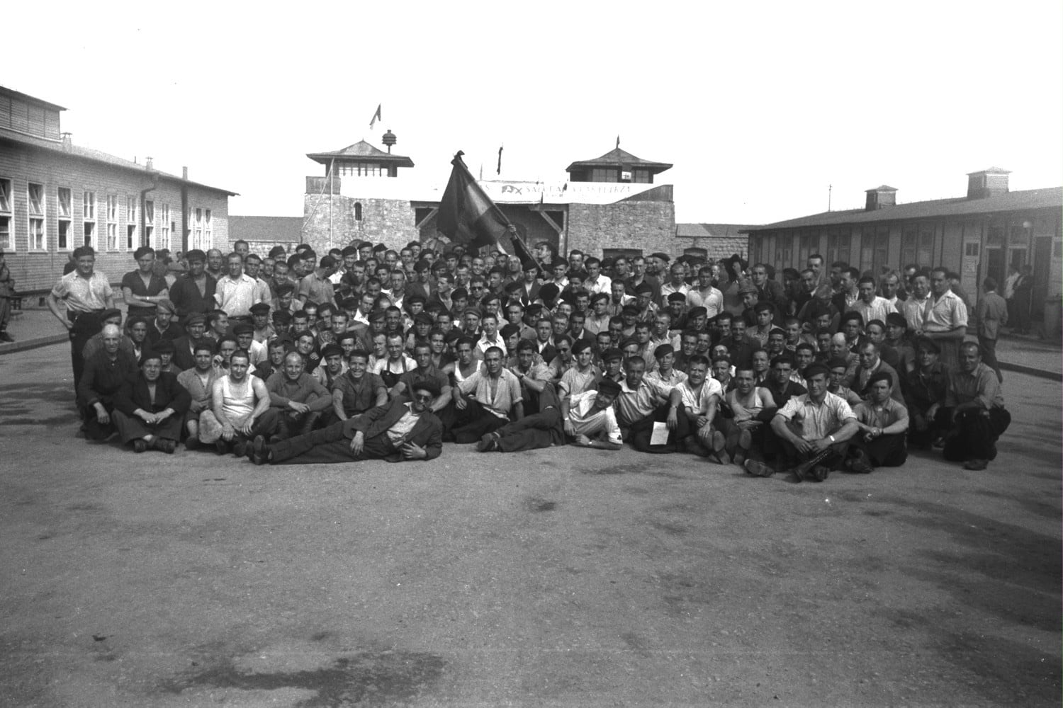 Grup de republicans supervivents a l’Appellplatz, davant de les torres d’entrada de Mauthausen. Per damunt dels seus caps oneja una bandera republicana. Maig de 1945. Fotografia de Francesc Boix. MHC. Fons Amical de Mauthausen-Francesc Boix Campo (amb el permís de la família Boix).