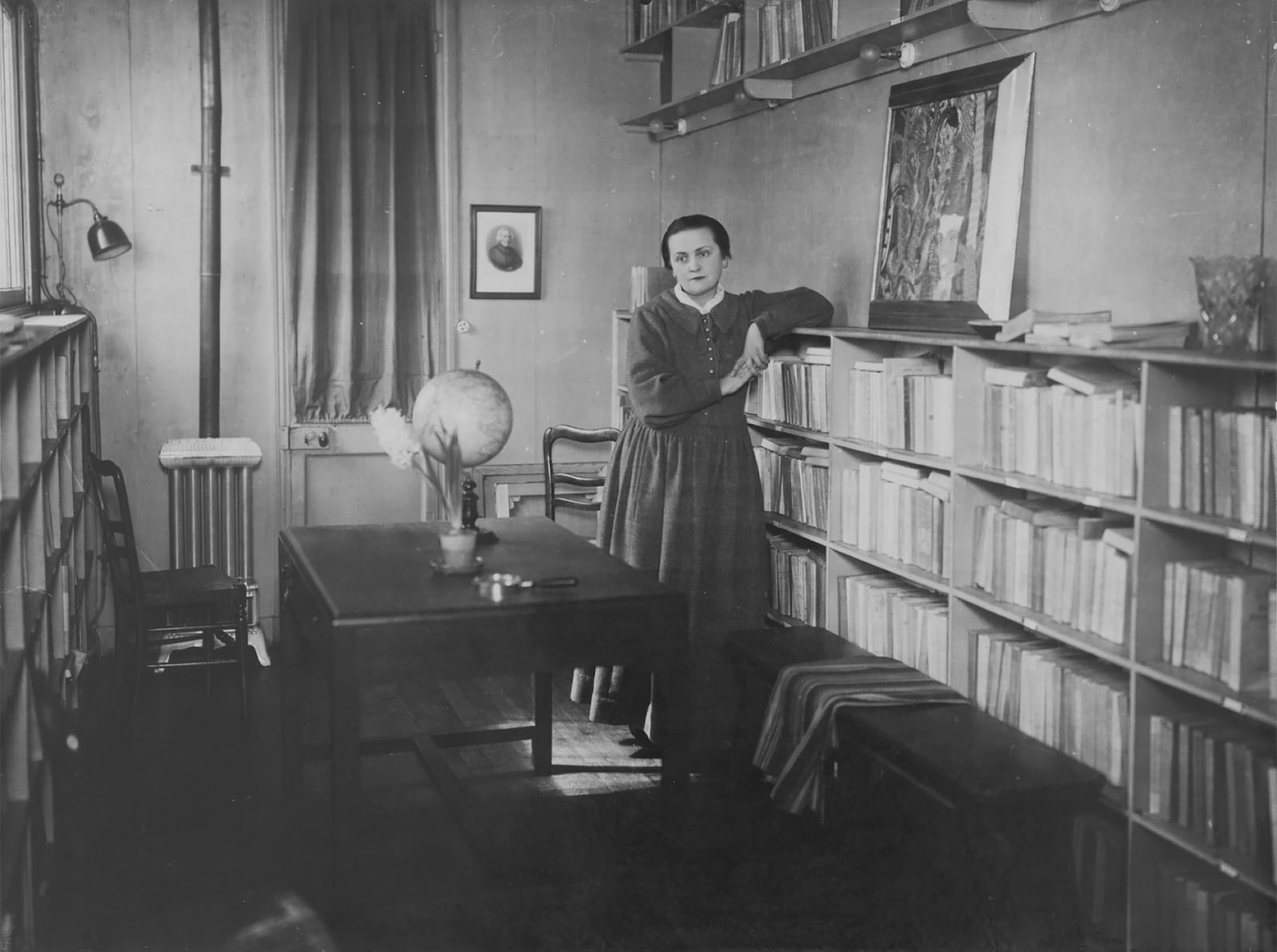 Adrienne Monnier apoyada en un estante de la rebotica de su librería. Fotografía de Henri Manuel, tomada alrededor de 1925. Bibliothèque Marguerite Durand. Ville de Paris.